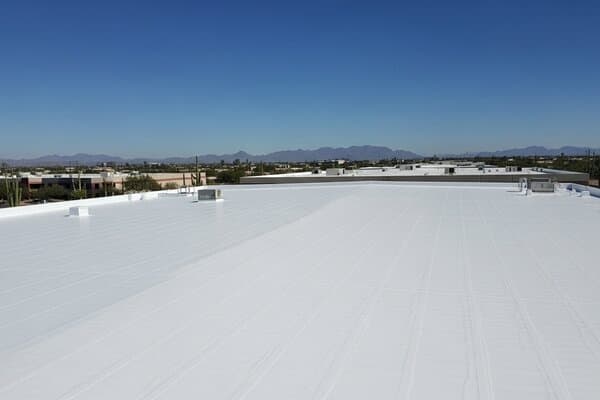 Phoenix Arizona commercial flat roof completely coated with white reflective silicone roof coating showing energy-efficient cool roof finish on warehouse building in Phoenix metro with desert landscape and blue sky