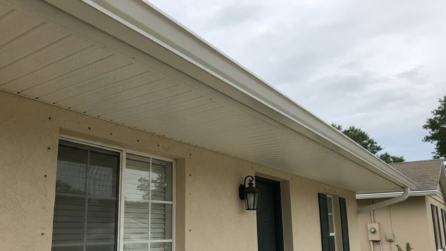 Orlando Florida soffit panel replacement contractor and homeowner standing in front of residential home with newly installed white vinyl soffit panels under roof eave Windermere Orange County suburban neighborhood tropical landscaping photograph